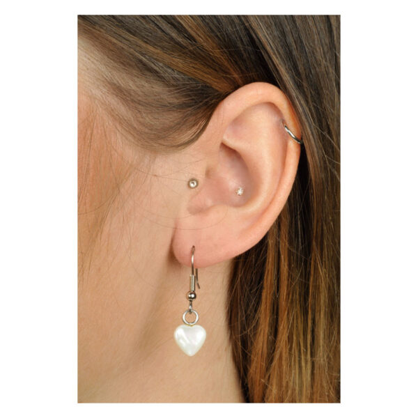 Pendientes de corazón blancos de plata en una oreja con cabello castaño
