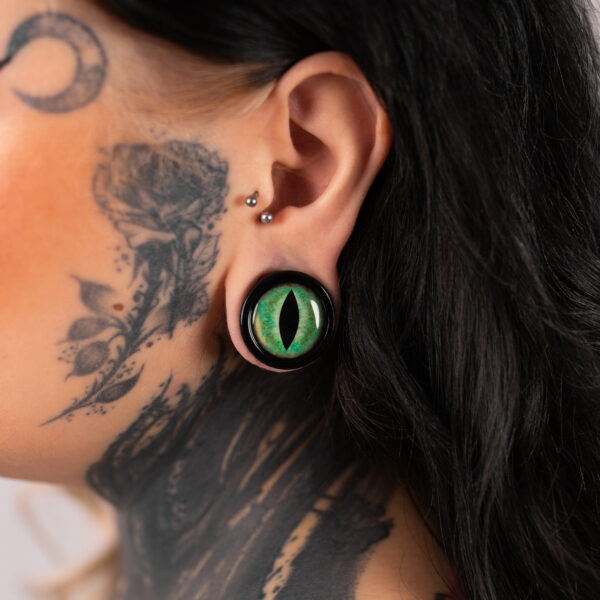Gran plug de ojo de gato verde en la oreja de una persona tatuada