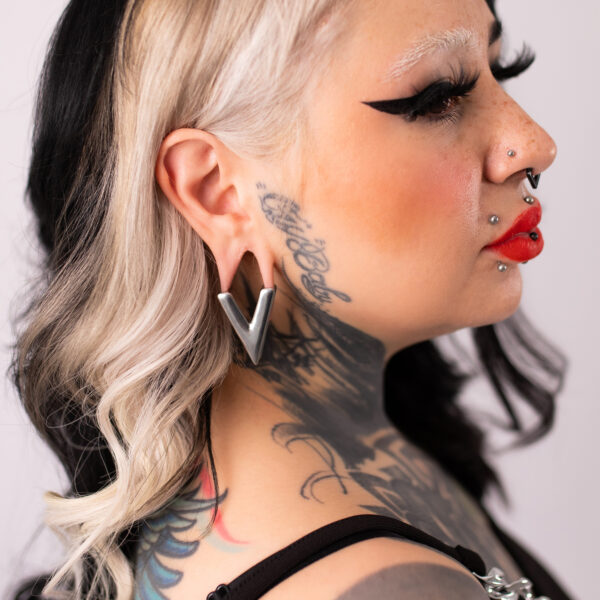 Mujer con pendiente en forma de V plateado, cabello negro, cuello tatuado