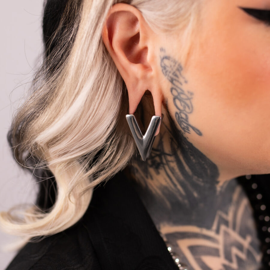 Pendiente plateado en forma de V en la oreja de una persona tatuada, perfil lateral