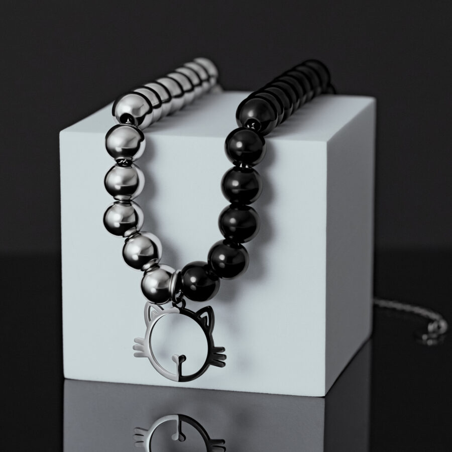 Collar de perlas plata-negro con colgante de gato sobre un cubo blanco
