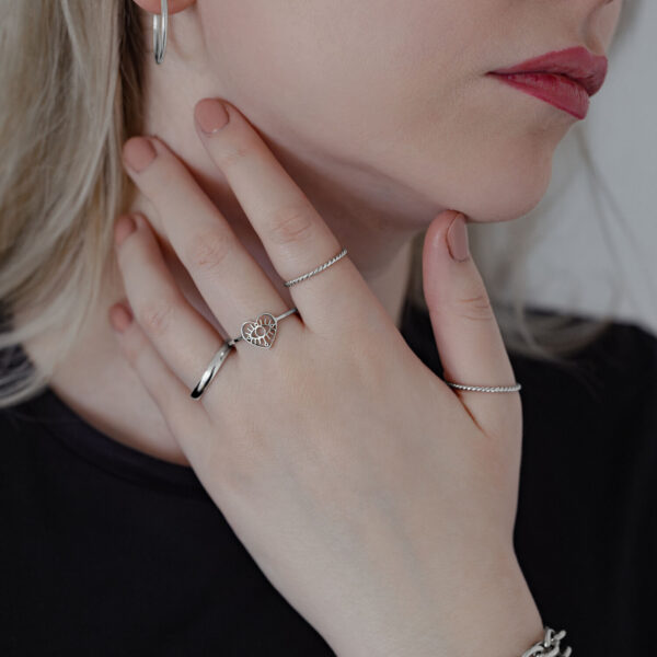 Mujer lleva varios anillos, incluido un Eye-Ring en plata sobre fondo claro