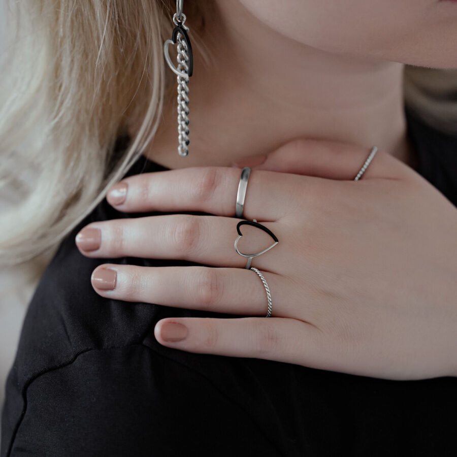 Primer plano de una mano con un anillo de corazón bicolor de acero quirúrgico, usado junto a otros anillos