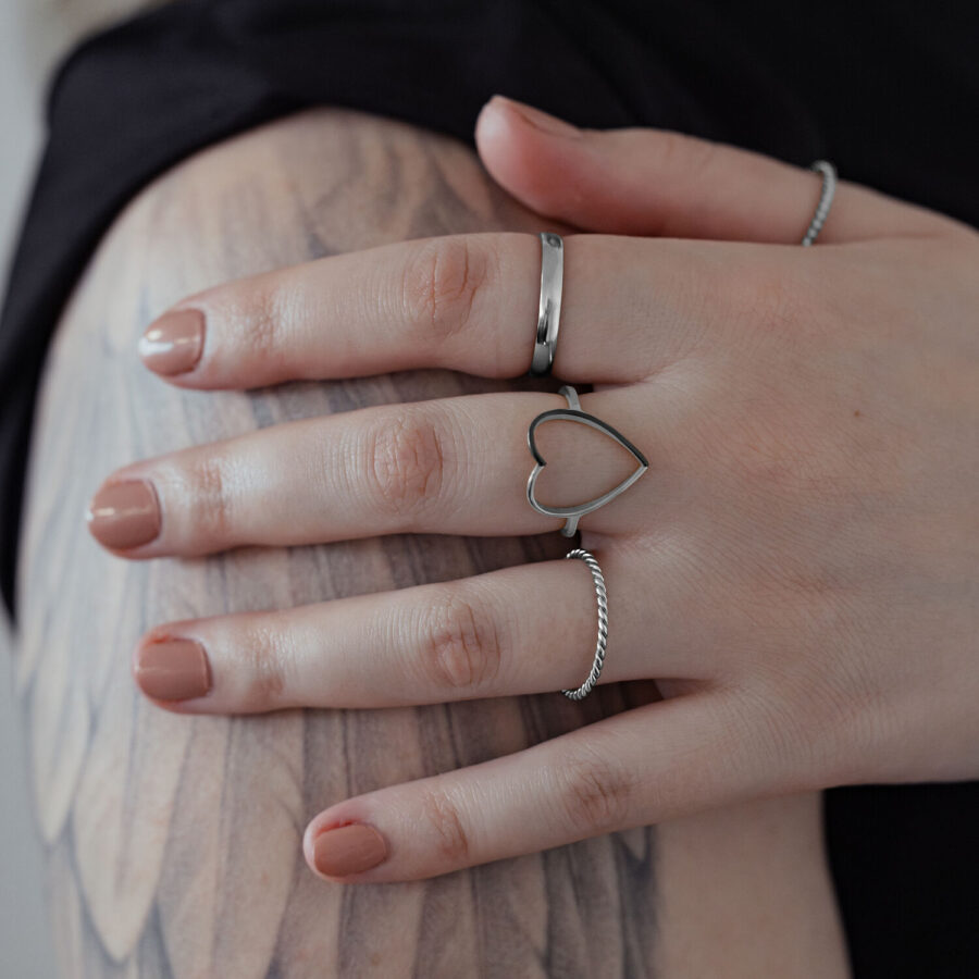 Anillo de corazón plateado de acero quirúrgico en una mano con brazo tatuado