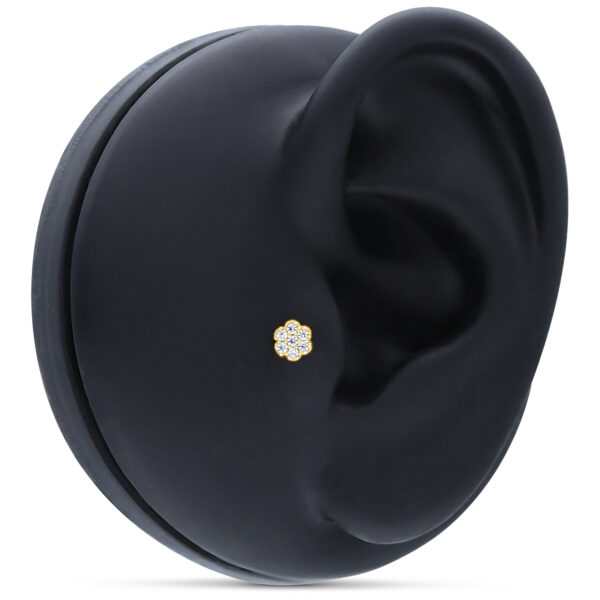 Accesorio dorado en forma de flor con cristales claros sobre modelo de oreja negro
