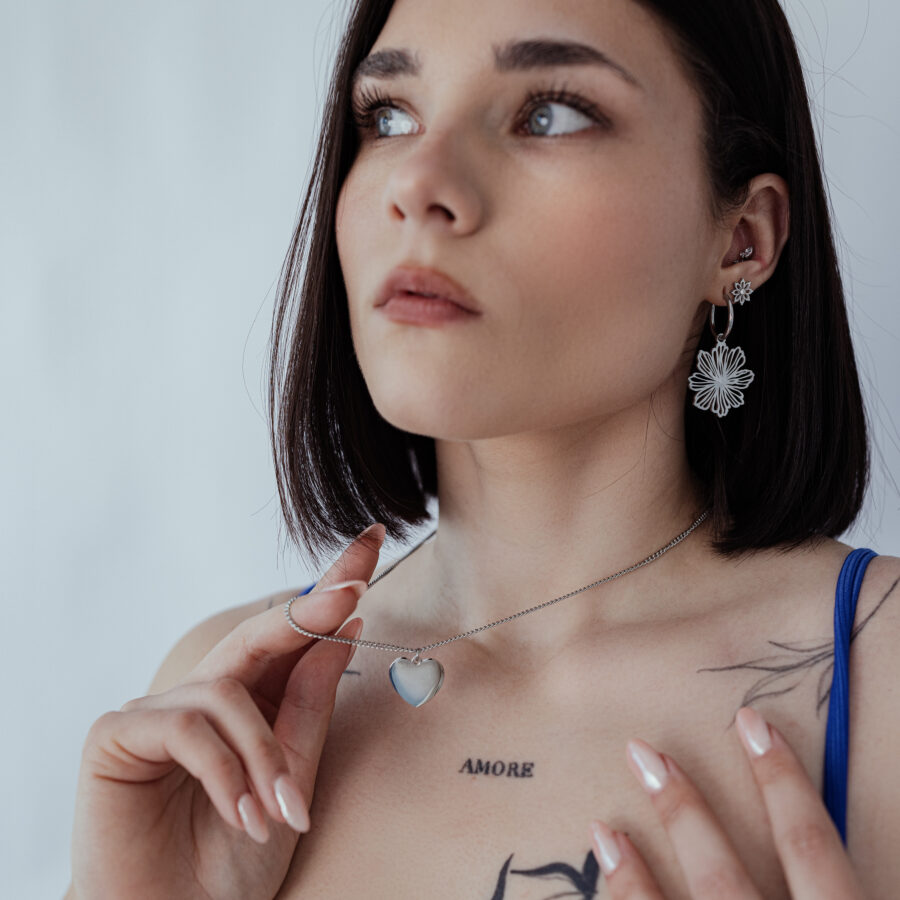 Mujer lleva collar plateado con colgante de corazón grabable sobre fondo neutro