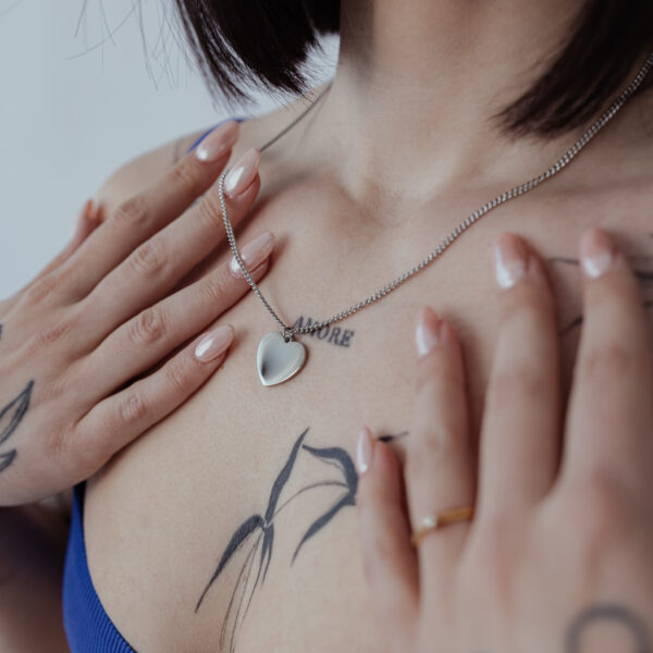 Cadena plateada con colgante de corazón grabable sobre piel con tatuajes