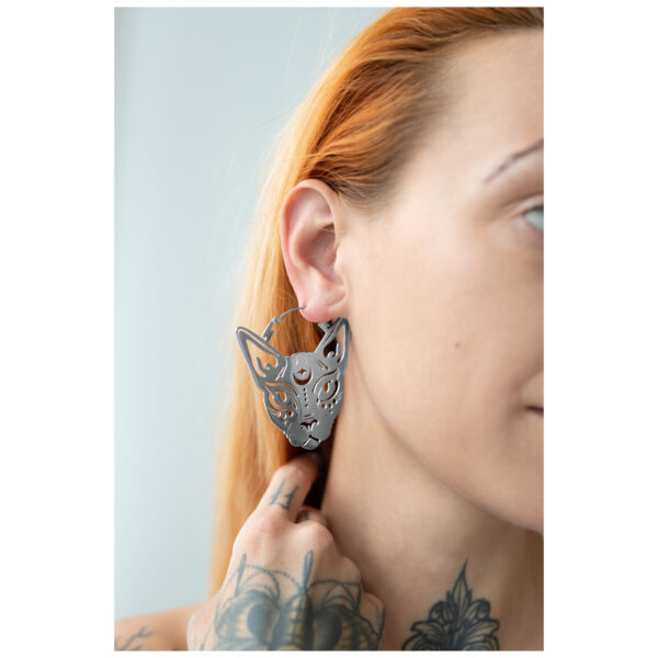 Pendientes Sphynx Hoops plateados en una oreja con mano tatuada