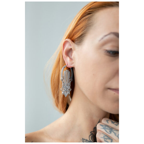 Mujer con pendientes Khamsa Hoops de acero quirúrgico en plata sobre fondo claro