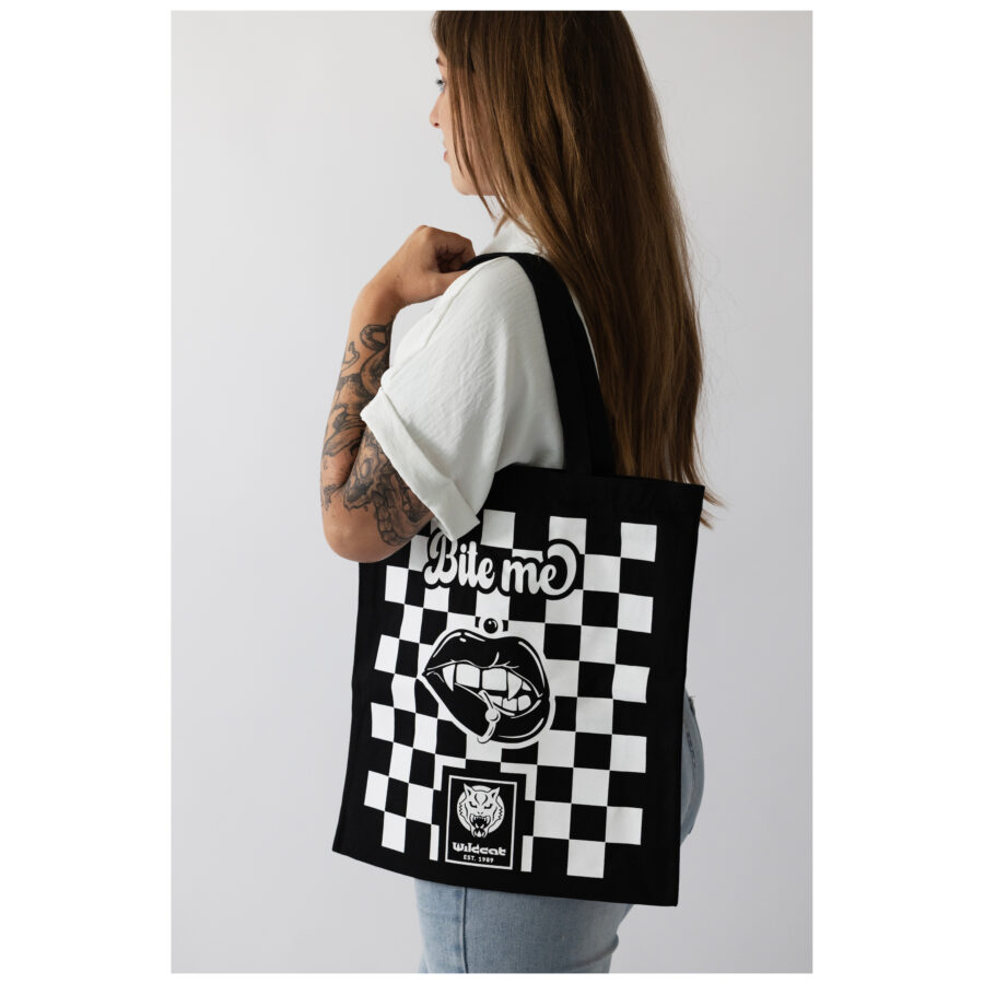 Mujer con bolsa de algodón negra, diseño de ajedrez y texto 'Bite Me'