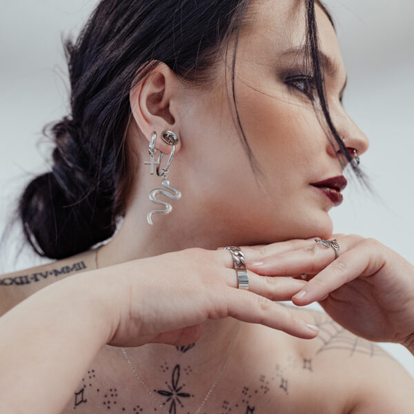 Mujer con aros Little Cross plateados y pendiente de serpiente, fondo blanco