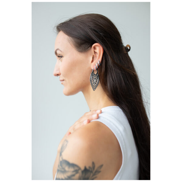 Mujer con cabello largo lleva pendientes Creek Hoops de plata sobre fondo neutro