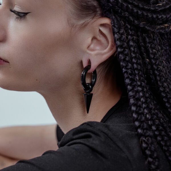 Primer plano de una persona con pesos para orejas Arrow negros de acero quirúrgico, cabello trenzado al fondo