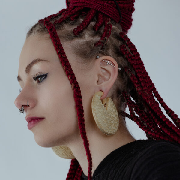 Persona con trenzas rojas lleva grandes pesas para orejas de madera Waves