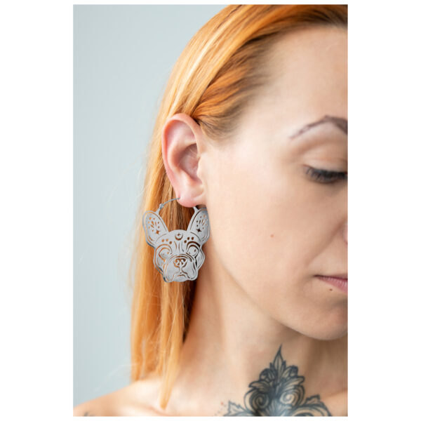 Aros de bulldog plateados en la oreja de una mujer con cabello claro y tatuaje