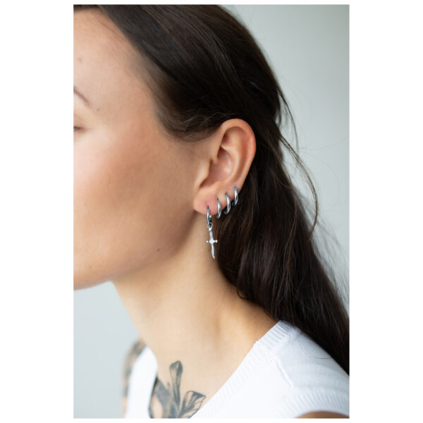 Pendientes de plata en forma de espada en oreja femenina sobre fondo neutro