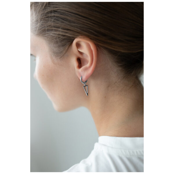 Aros triangulares negros y plateados en la oreja de una persona con cabello castaño, fondo blanco