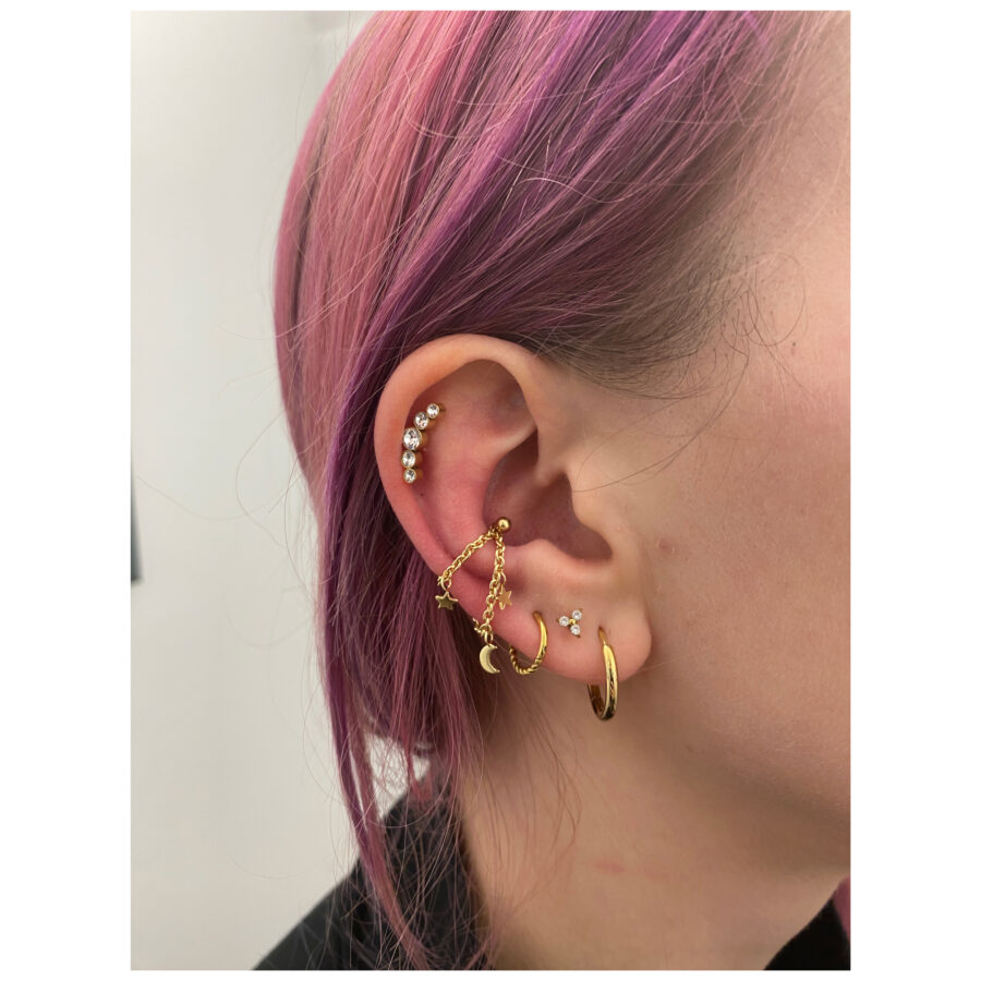 Cadena de piercing dorada con motivos de luna y estrellas llevada en la oreja