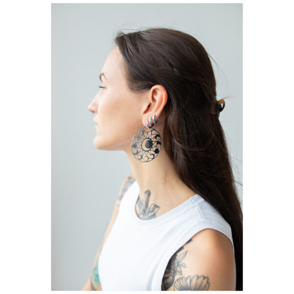 Mujer con cabello largo y oscuro lleva grandes pendientes redondos con diseño de luna sobre un fondo gris