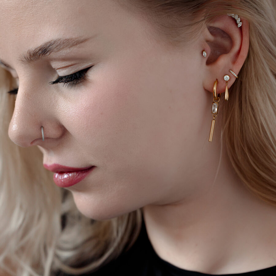 Mujer con varios piercings, incluyendo una punta de piercing de cristal dorado en la oreja.