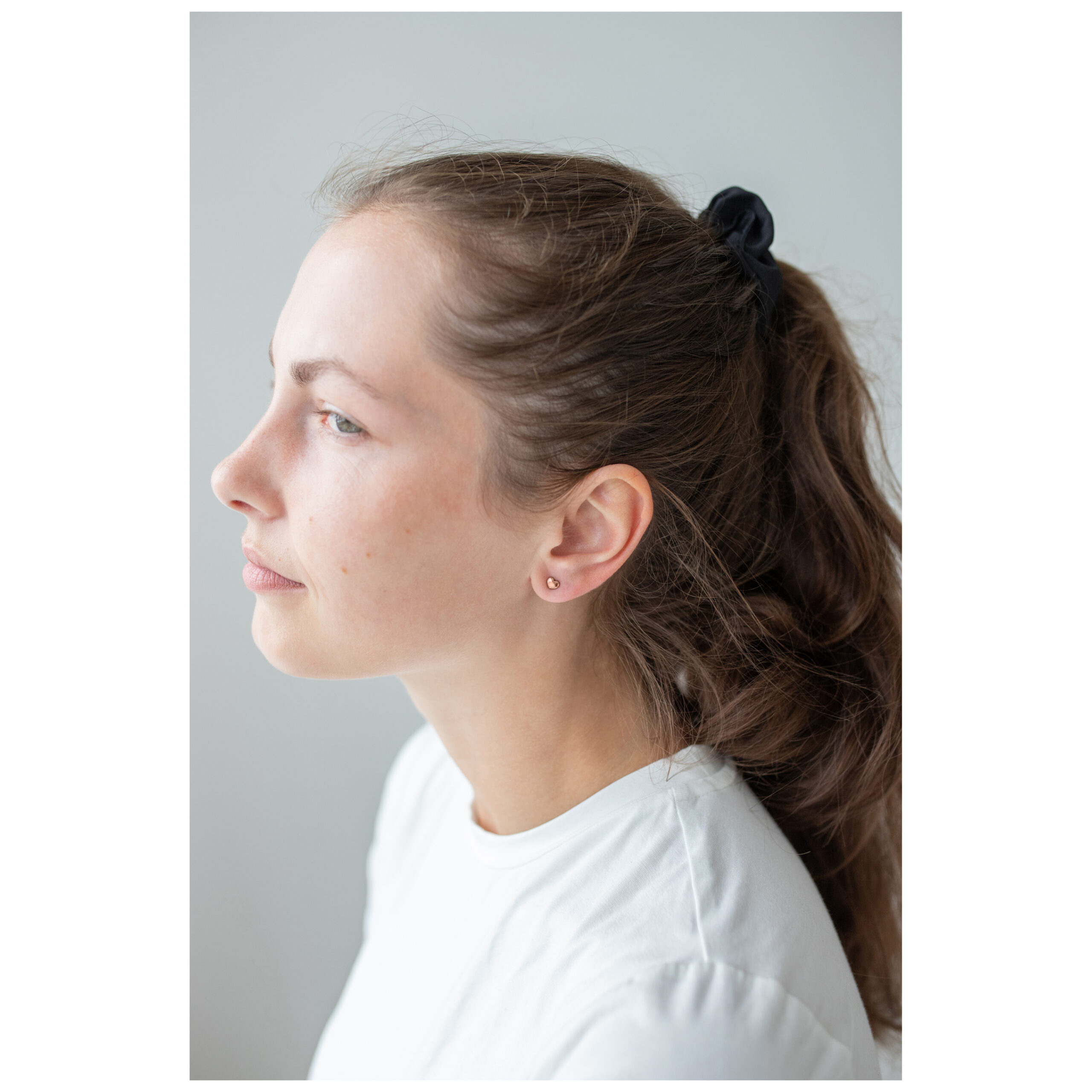 Roségold Herz Ohrstecker am Ohr Frau mit Roségold Herz Ohrstecker, Haare im Zopf, weißes Oberteil