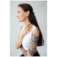 Mujer con cabello largo lleva aros Little Anchor dorados, perfil lateral