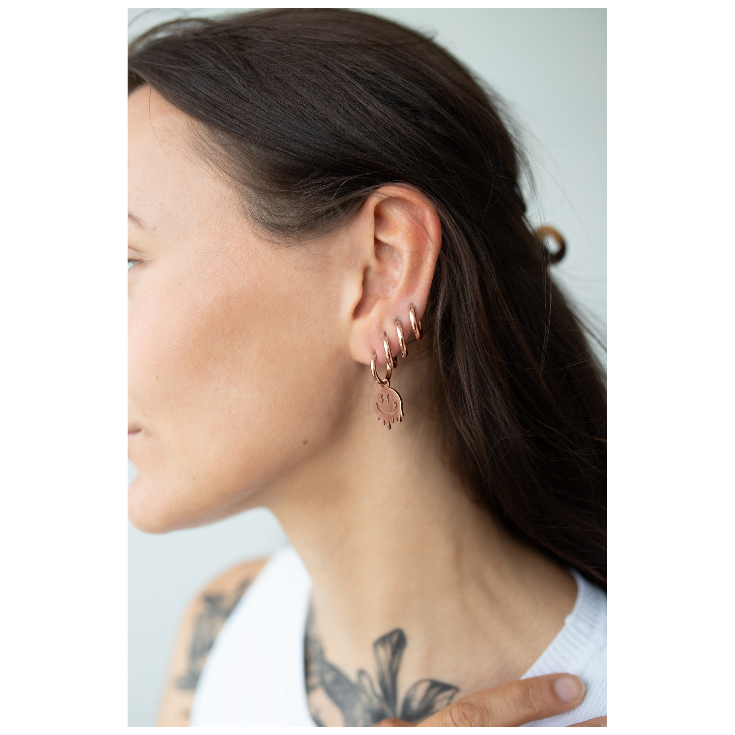 Frau mit roségoldenen Smiley-Ohrringen aus Chirurgenstahl am Ohr.