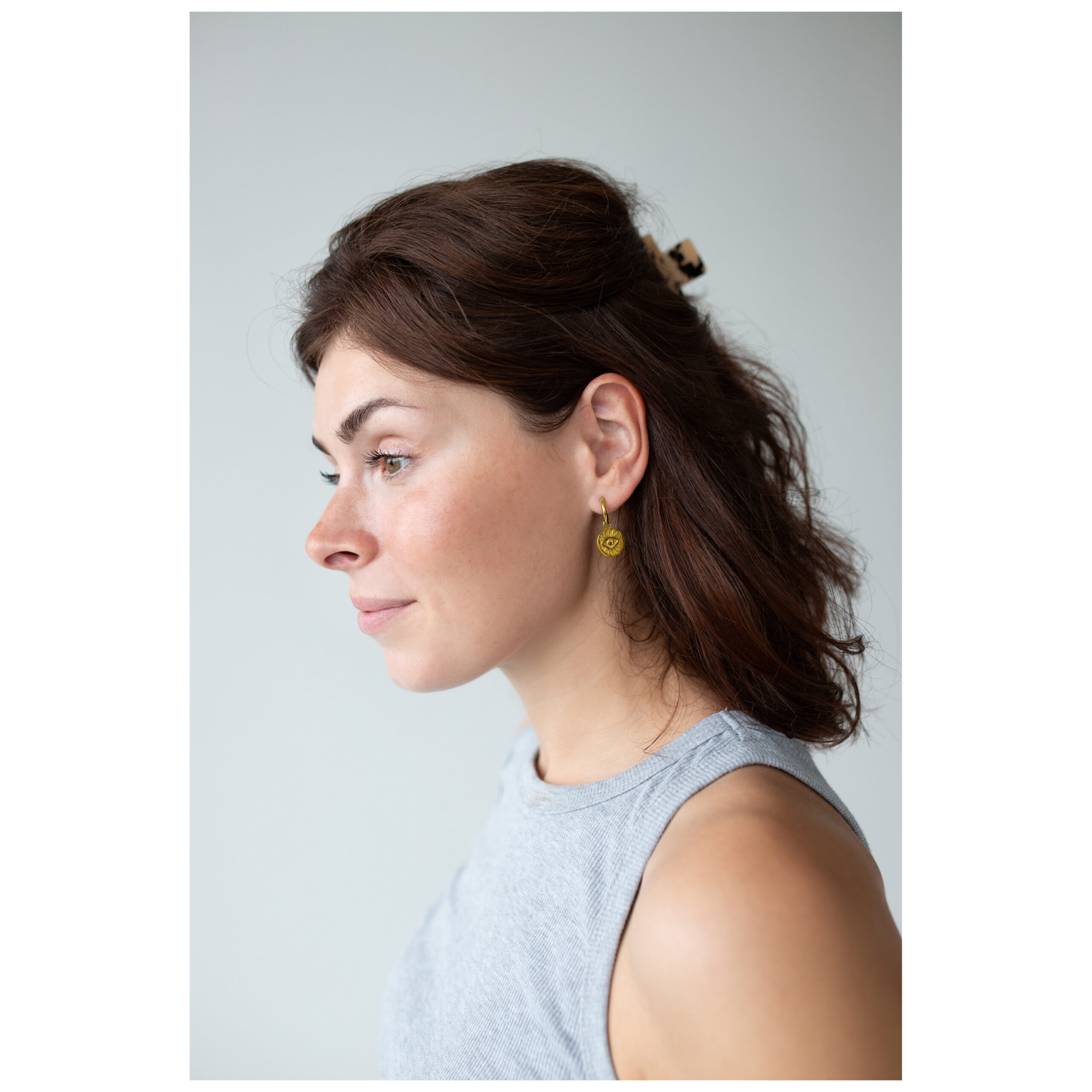 Mujer lleva aros dorados Little Luminous Eye Hoops frente a fondo gris