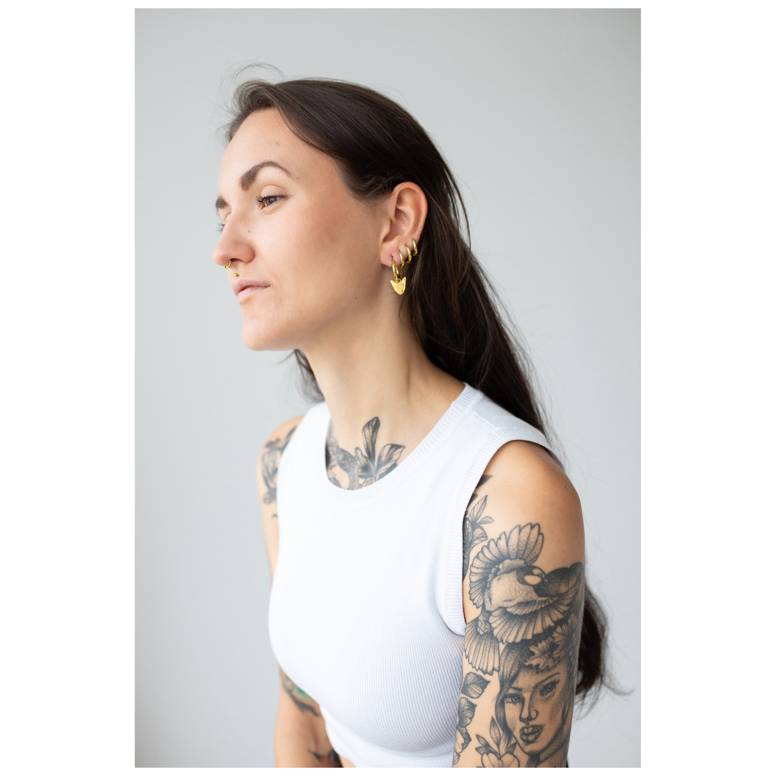 Mujer con aros Little Sphynx de oro, brazo tatuado, top blanco