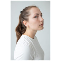 Mujer con pendientes Little Daisy Hoops dorados frente a un fondo blanco