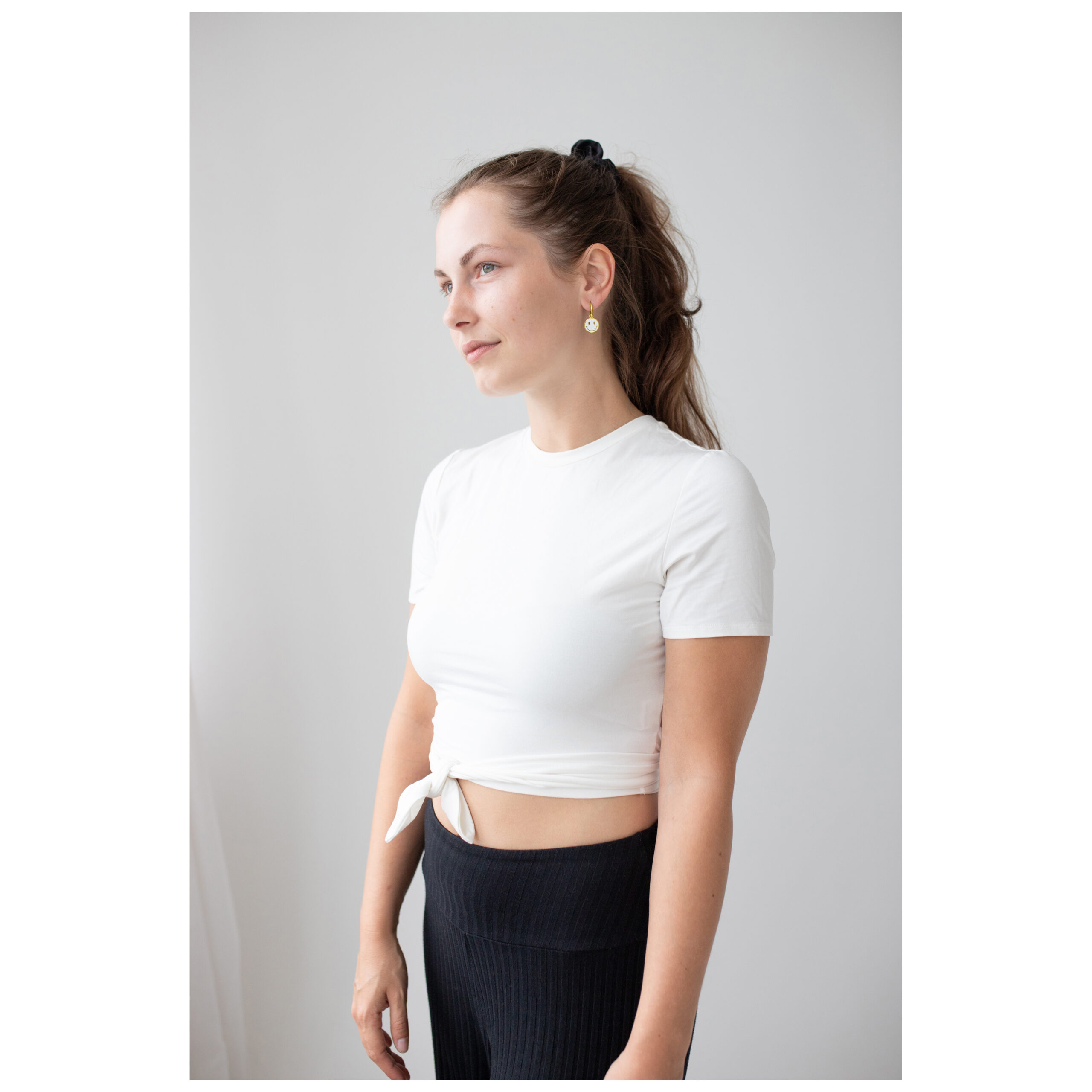 Mujer con aros dorados Smiley y camiseta blanca frente a un fondo neutro