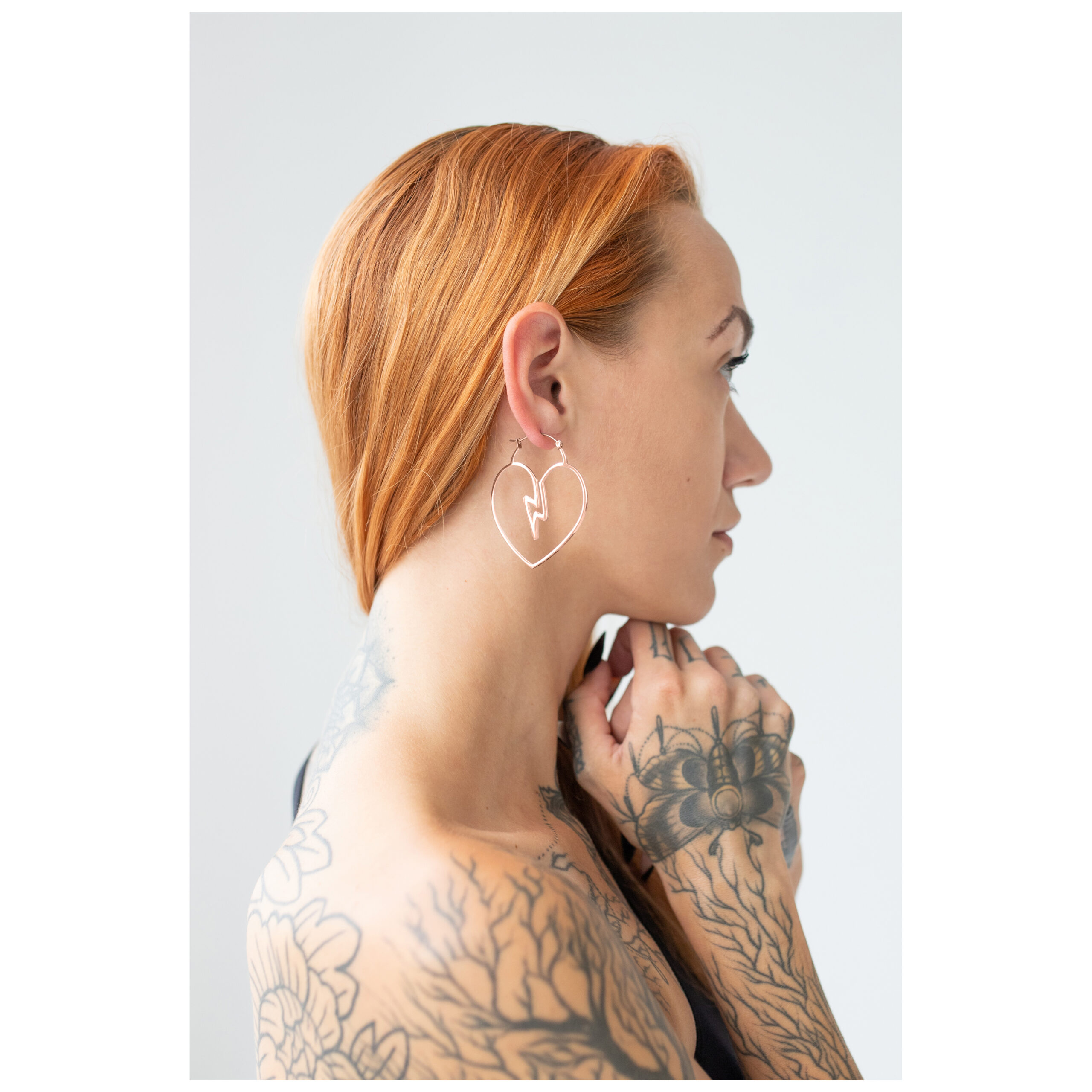 Roségoldene Heartbreaker Hoops Ohrringe Frau mit roten Haaren trägt roségoldene Herz-Ohrringe vor weißem Hintergrund