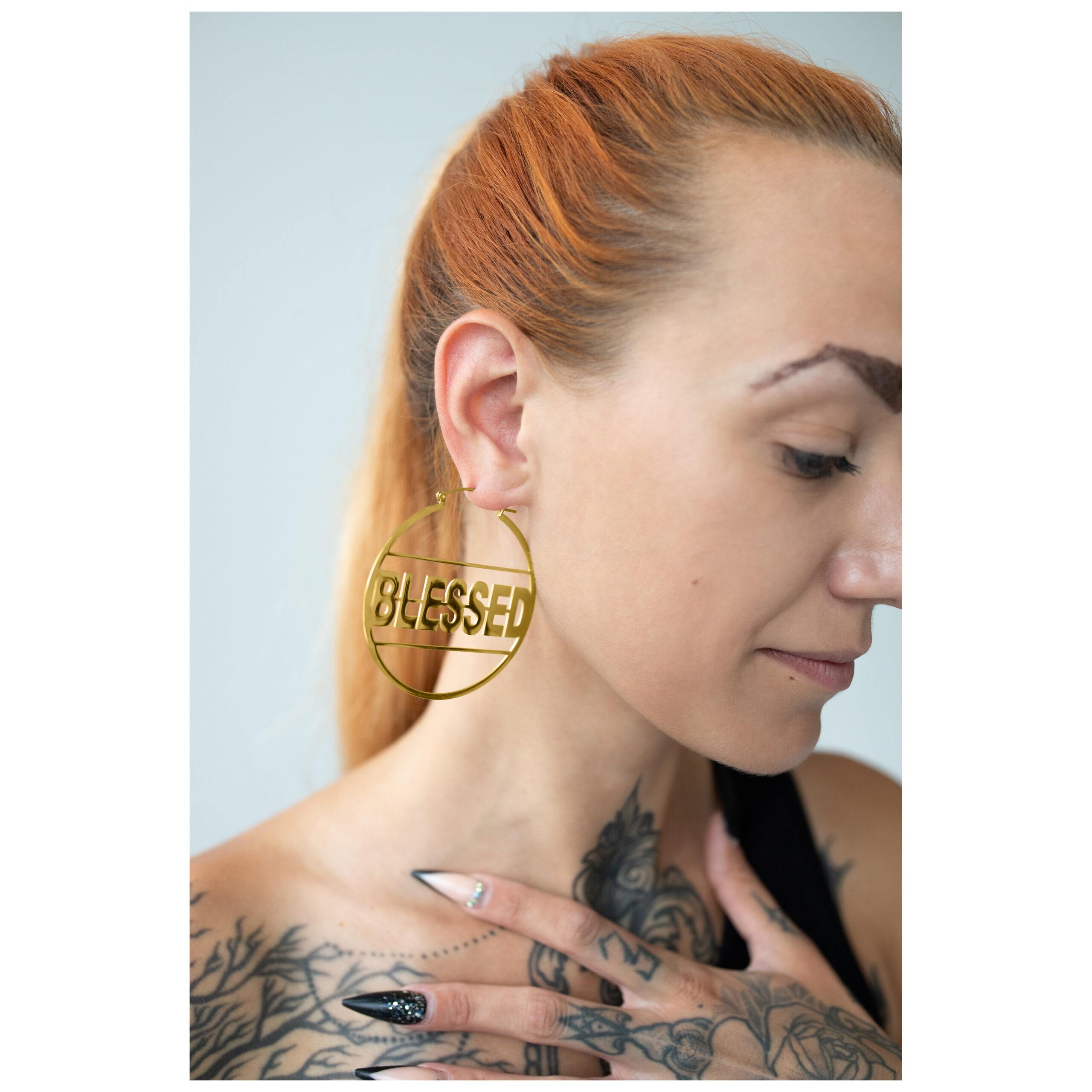Mujer con aros Blessed dorados y tatuajes, perfil lateral