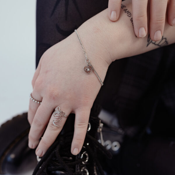 Pulsera delicada de plata con detalle de corazón, llevada en la muñeca de una persona.