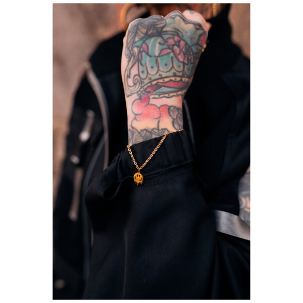 Pulsera dorada con colgante de Smiley en muñeca tatuada