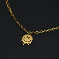 Pulsera dorada con colgante de carita sonriente sobre fondo negro