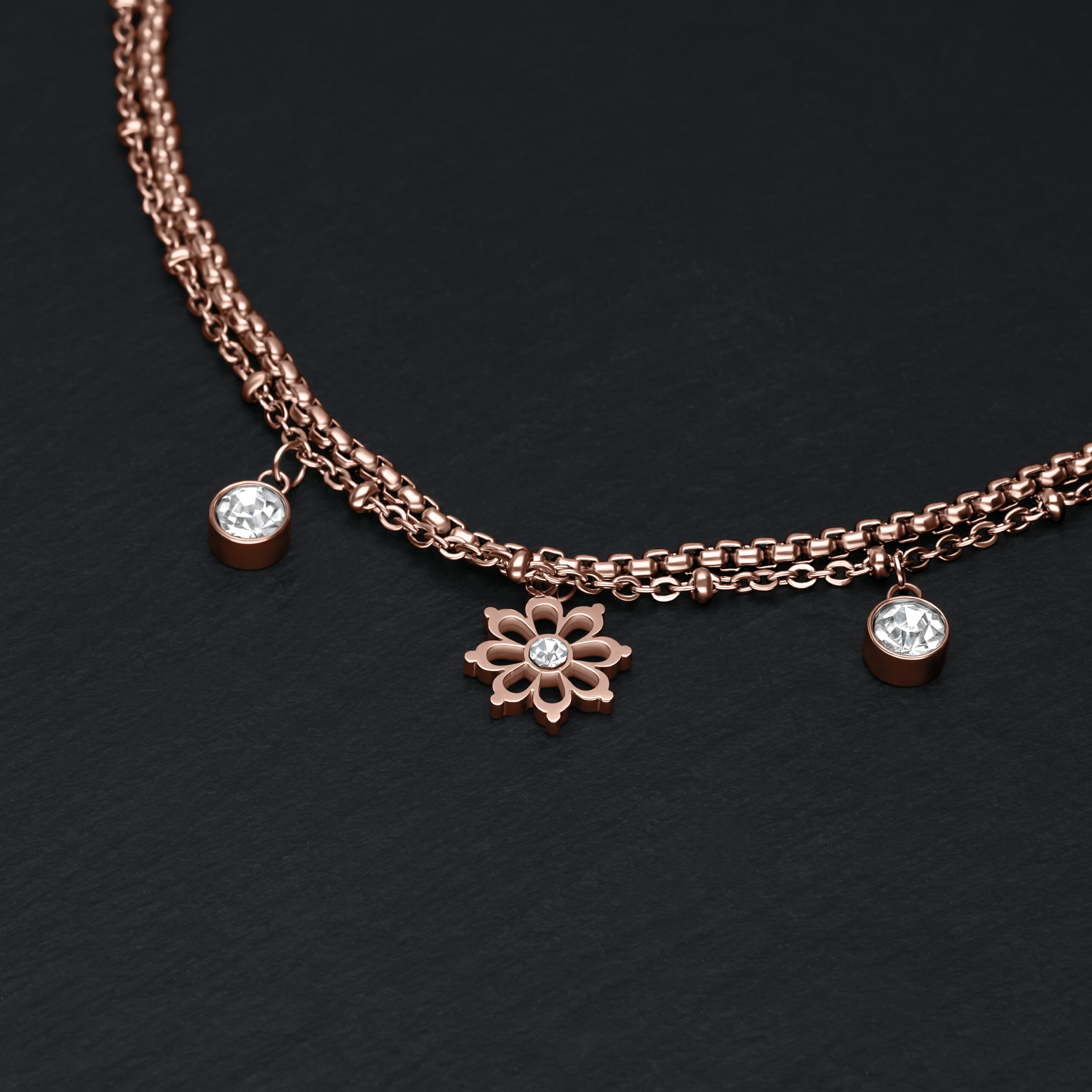 Roségoldenes Armband mit Blumenanhänger und klaren Kristallen auf schwarzem Hintergrund