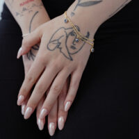 Pulsera dorada Little Nazar en una muñeca tatuada sobre fondo negro