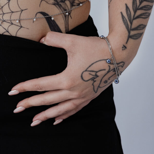 Pulsera de plata con colgante Nazar en la muñeca, mano tatuada