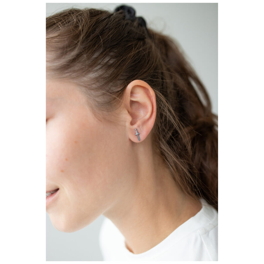 Pendientes de espada plateados en la oreja de una mujer sobre un fondo claro