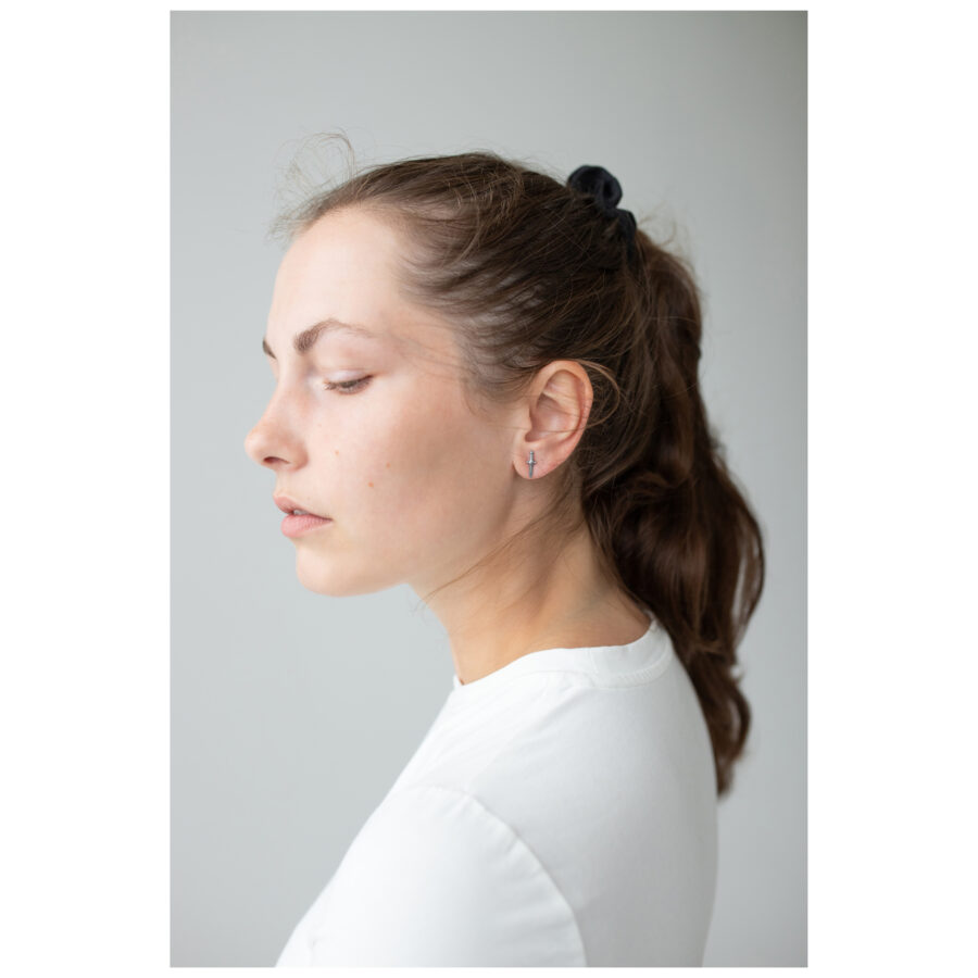 Mujer con cabello largo lleva elegantes pendientes de espada en plata sobre fondo gris