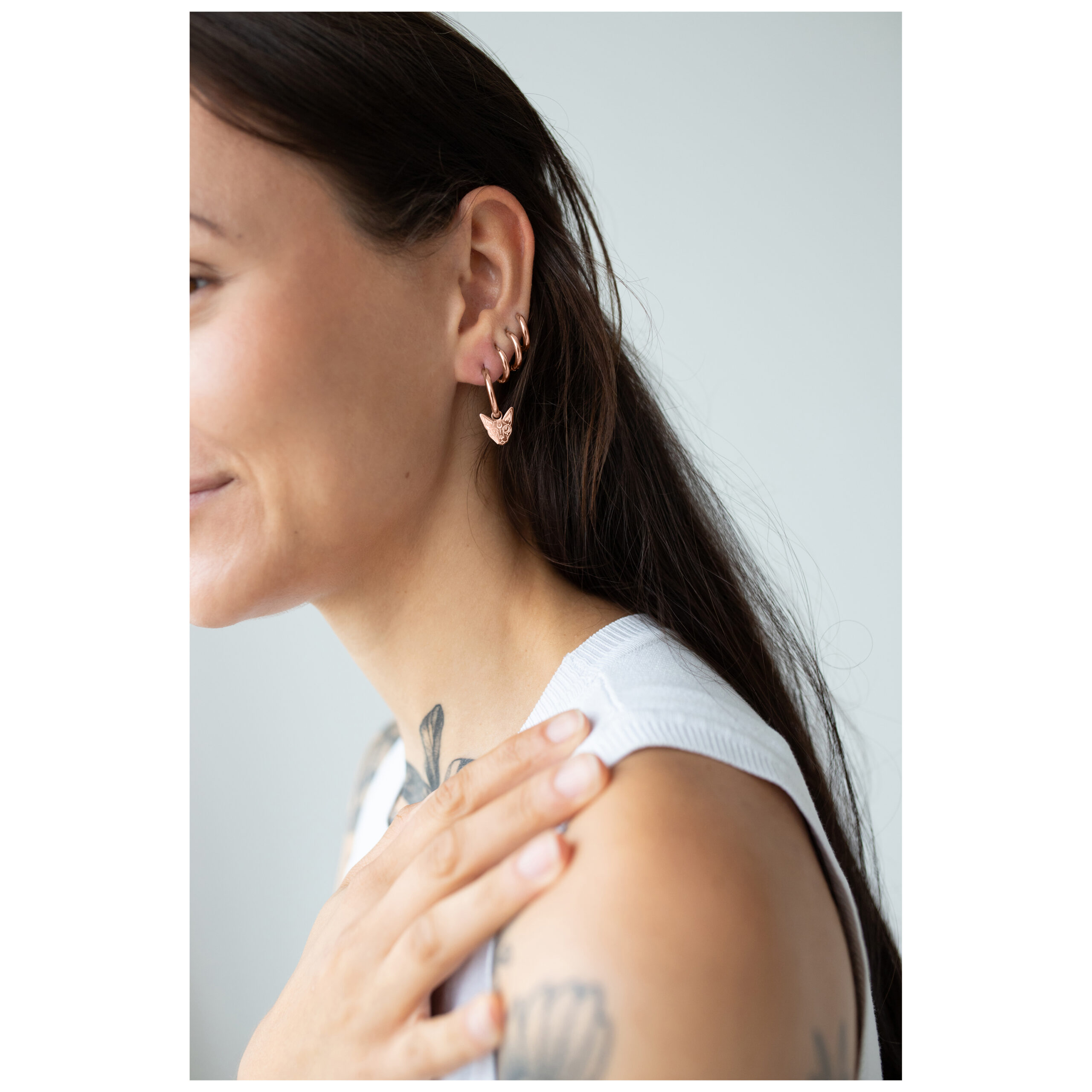 Roségoldene Little Sphynx Hoops Ohrringe Roségoldene Ohrringe an einem Ohr, getragen von einer Frau mit braunem Haar