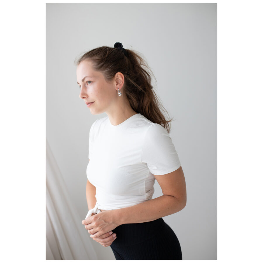 Mujer con camiseta blanca y elegantes pendientes de plata sobre fondo neutro