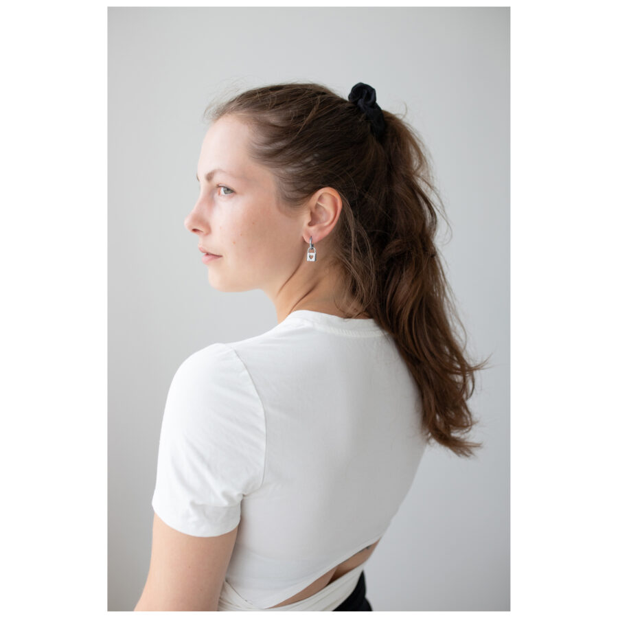 Mujer con cabello largo lleva pendientes Little Lock Hoops en plata sobre fondo blanco