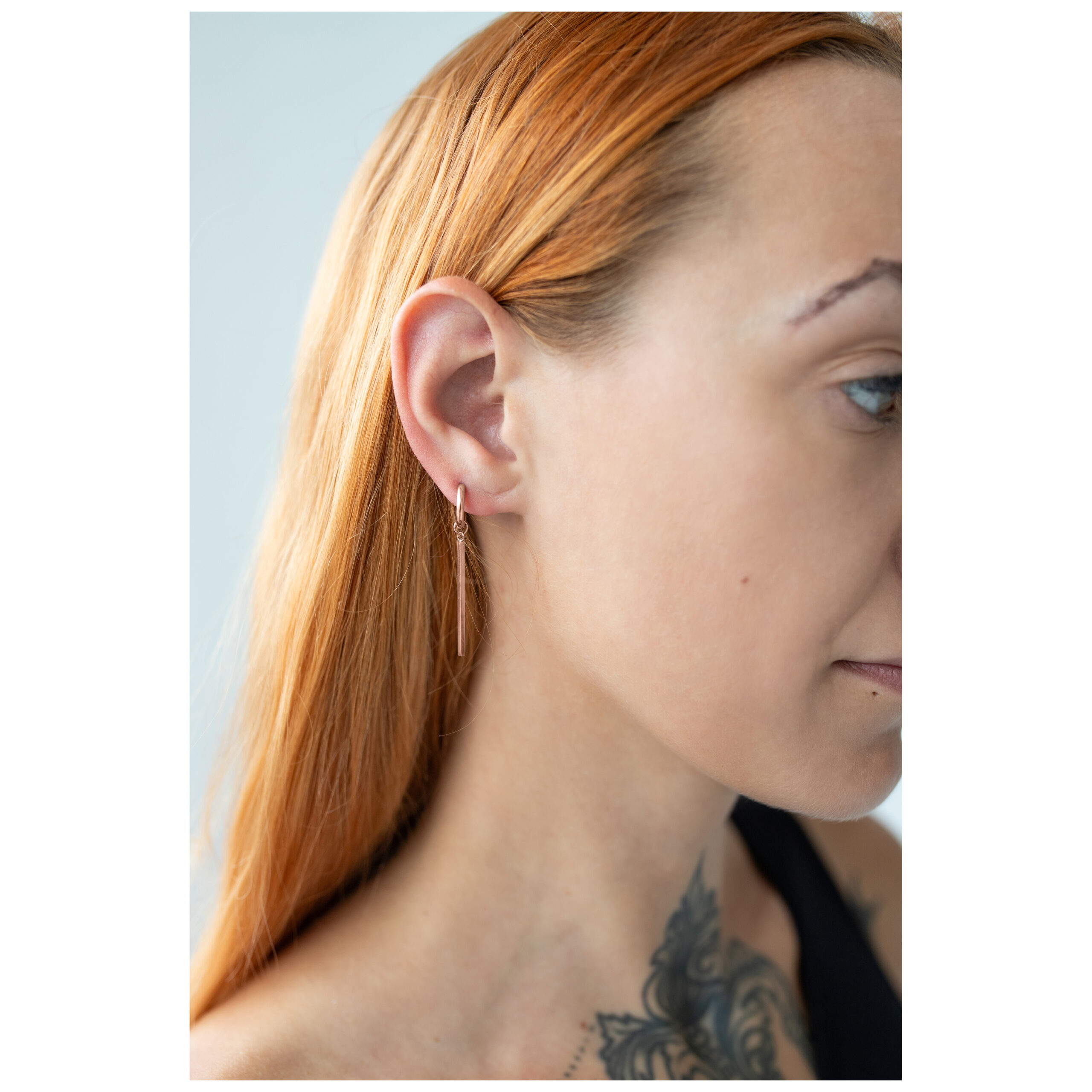 Roségoldene Ohrringe am Ohr einer Frau mit langem Haar
