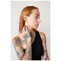 Person mit tätowiertem Arm trägt roségoldene Little Bar Hoops Ohrringe