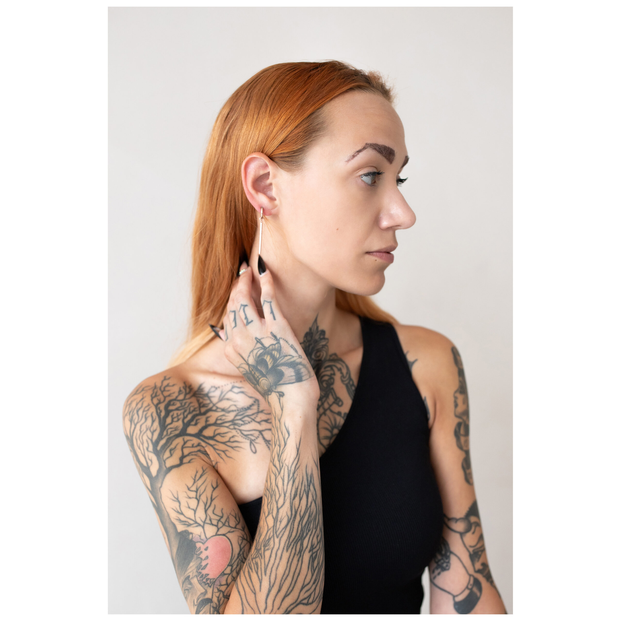 Person mit tätowiertem Arm trägt roségoldene Little Bar Hoops Ohrringe