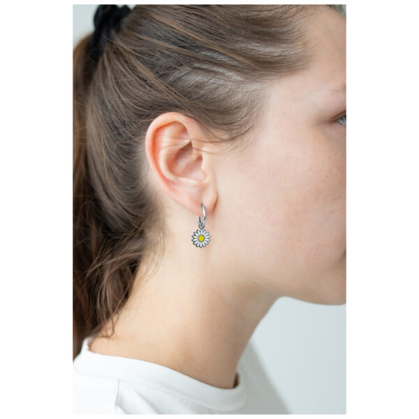 Pendientes plateados con diseño de margarita en una oreja con cabello castaño