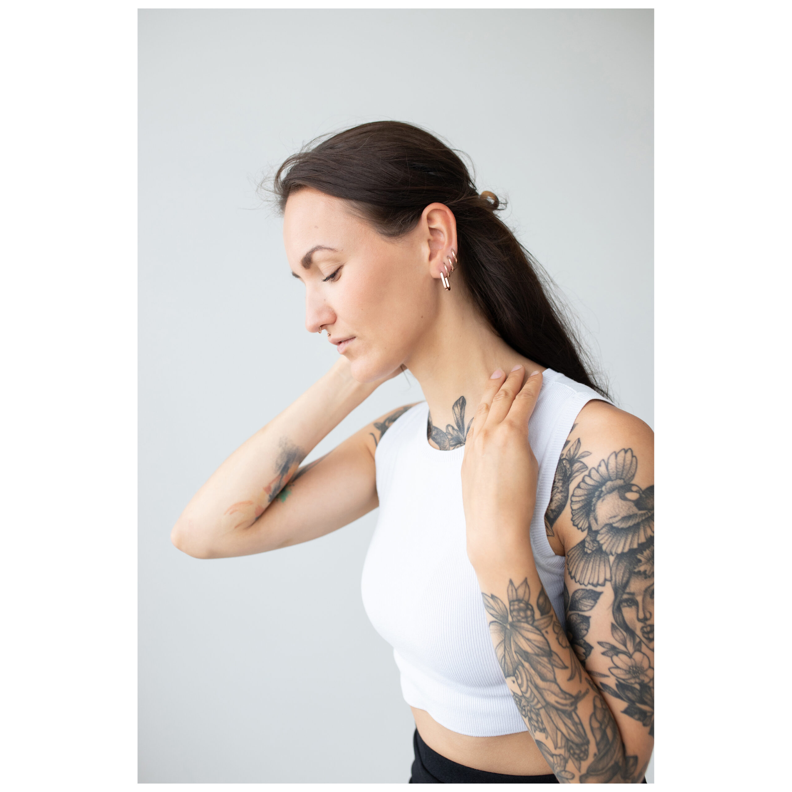 Frau mit tätowierten Armen trägt Roségold Ohrringe vor grauem Hintergrund