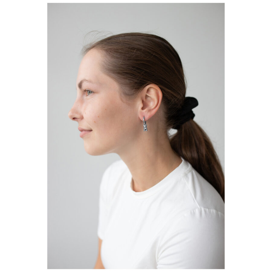 Mujer con cabello castaño lleva pendientes de ositos de goma negros, camiseta blanca.